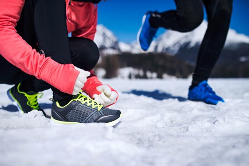 Due runners in un paesaggio innevato, uno mentre si allaccia una scarpa