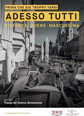 Scattata nell'aprile 2020, la fotografia in bianco e nero mostra Piazza Duomo di Bressanone senza vita, con le sedie appoggiate sui tavoli. L’immagine è accompagnata dallo slogan: Prima che sia troppo tardi. Adesso tutti. Distanza, igiene, mascherina