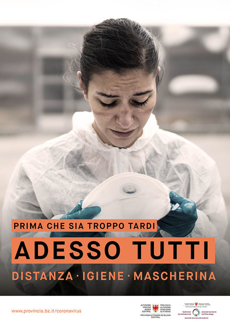 Una dottoressa o forse un’infermiera esausta, col volto segnato, contempla la sua mascherina. L’immagine è accompagnata dallo slogan: Prima che sia troppo tardi. Adesso tutti. Distanza, igiene, mascherina.