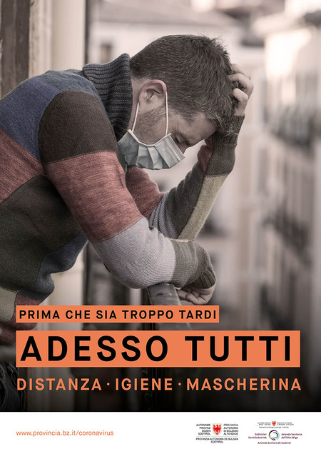 Pensieroso, in balcone, un uomo con la mascherina si gratta il capo. L’immagine è accompagnata dallo slogan: Prima che sia troppo tardi. Adesso tutti. Distanza, igiene, mascherina.