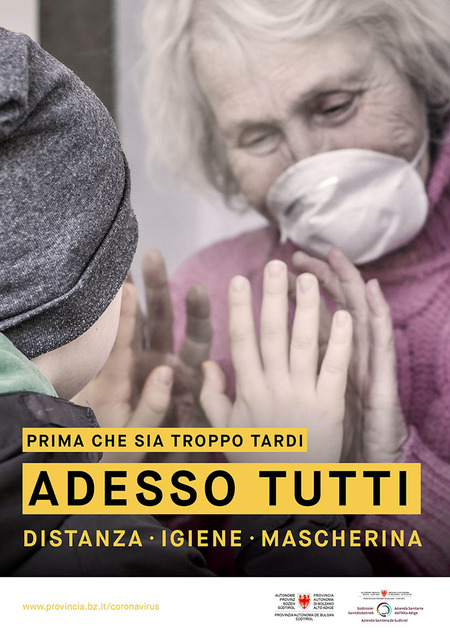 La nonna e il nipote separati da un vetro. Si vorrebbero abbracciare ma non possono. L’immagine è accompagnata dallo slogan: Prima che sia troppo tardi. Adesso tutti. Distanza, igiene, mascherina.